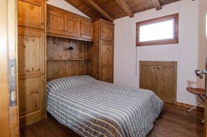 A bedroom with a wooden bed, a window, and built-in wooden cabinets. - Summer in the mountains (San Vito di Cadore)