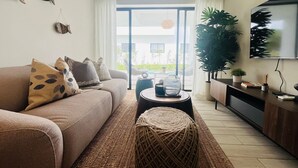 Un salon moderne avec un canapé, une table basse, un téléviseur et une vue sur une piscine et la verdure environnante.