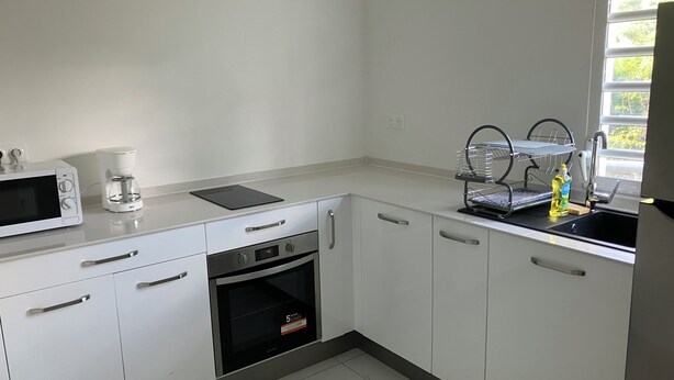A modern kitchen with white cabinets, a built-in oven, a microwave, a coffee maker, and a dish rack by the sink. - Studio 5 minutes from Sainte Anne beaches and hiking trails (Sainte-Anne)