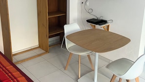 A compact room with a bed, a wooden wardrobe, a TV mounted on the wall, a small table with chairs, and a tiled floor. - Studio 5 minutes from Sainte Anne beaches and hiking trails (Sainte-Anne)