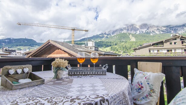 A balcony with a table set for two, overlooking a mountainous landscape with a construction crane in the background.