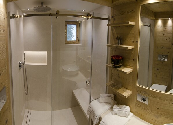 Een moderne badkamer met een douchecabine van glas, een rond wastafel en houten planken met toiletartikelen.