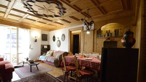 A cozy room with a wooden ceiling, a dining table set with a red and white checkered tablecloth, and a bed with a red blanket.