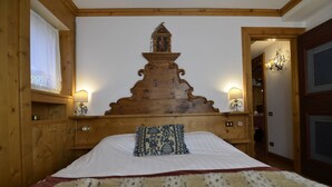 A wooden-framed bedroom with a large bed, a decorative headboard, and a window with a white curtain.