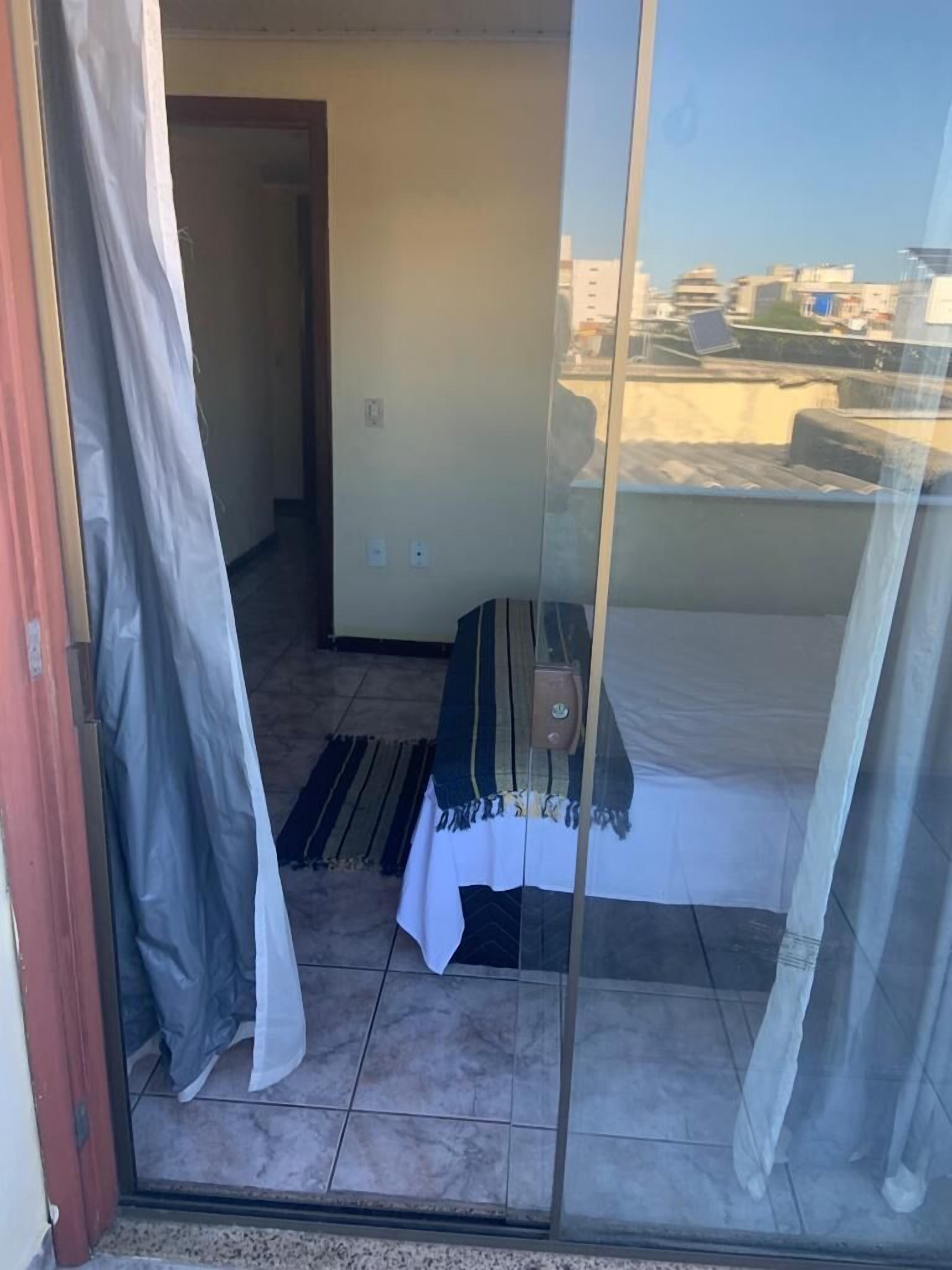 Quarto com cama, uma mesinha e vista da cidade através de uma porta de vidro.