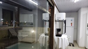Eine moderne Küche mit weißen Schränken, einem Kühlschrank, einer Kaffeemaschine und einer Glastrennwand.