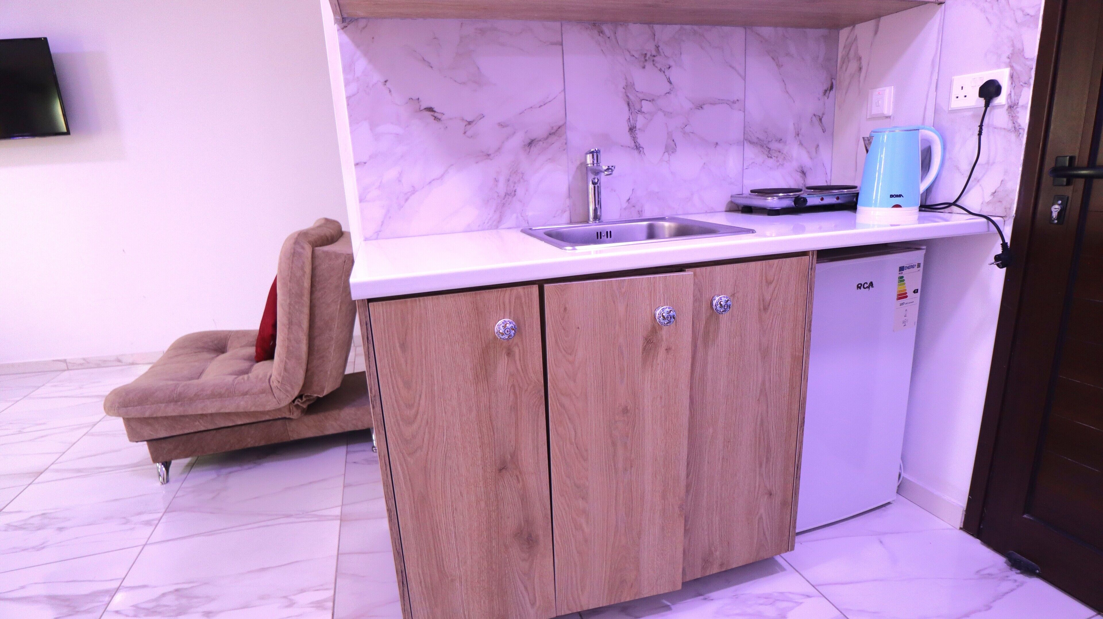 A compact kitchen with a marble backsplash, wooden cabinets, a sink, and a coffee maker.
