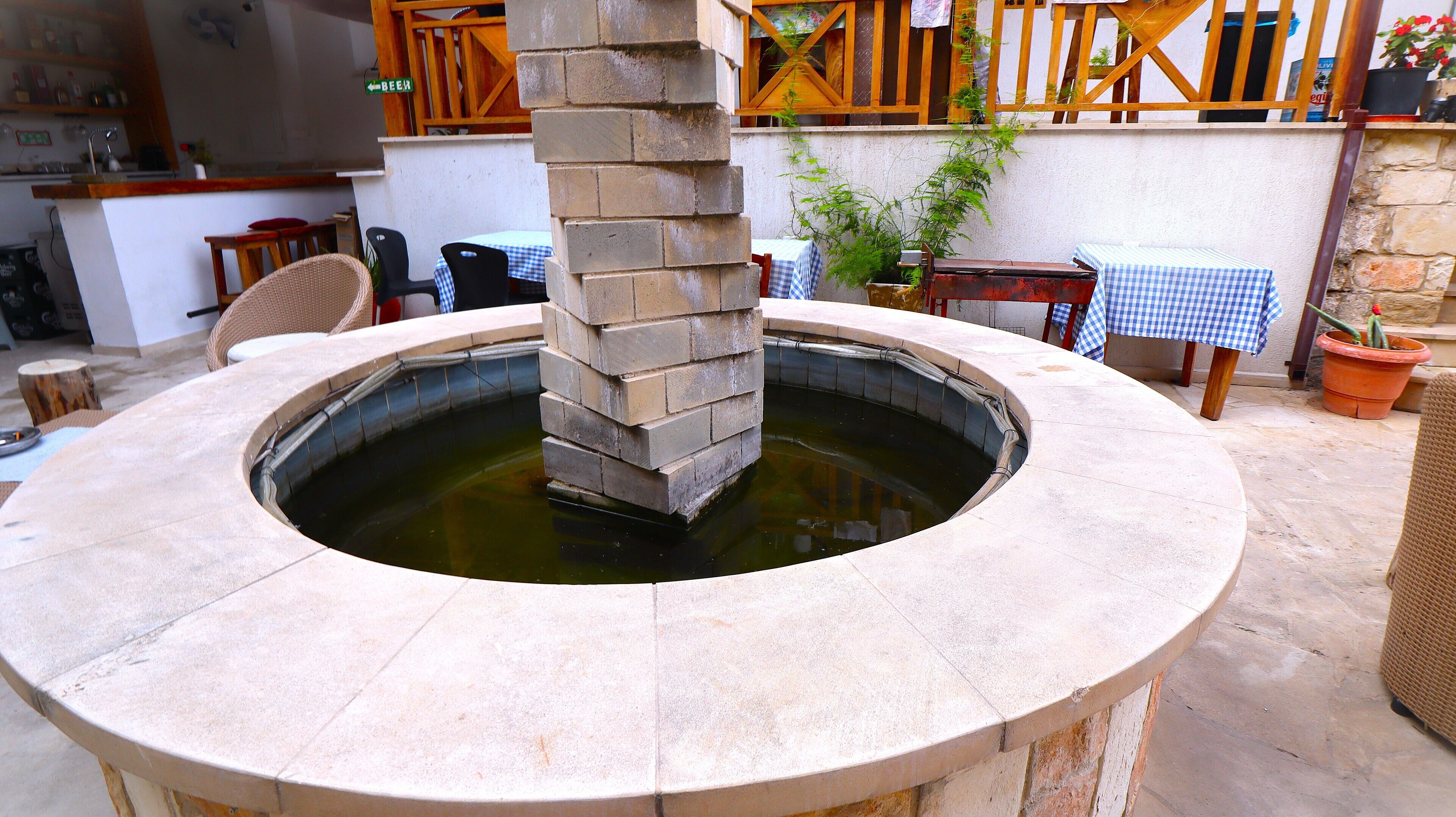 Una fuente de piedra con un recipiente circular, rodeada de asientos exteriores y una valla de madera.