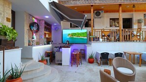 Ένας χώρος με μπαρ, τηλεόραση, έπιπλα από ξύλο και διακοσμητικά φυτά σε γλάστρες.