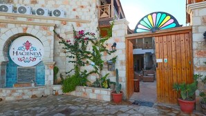 Η είσοδος ενός ξενοδοχείου με μια ξύλινη πύλη, μια πινακίδα που γράφει «Hacienda Cyprus» και μια πρόσοψη κτιρίου από πέτρα.