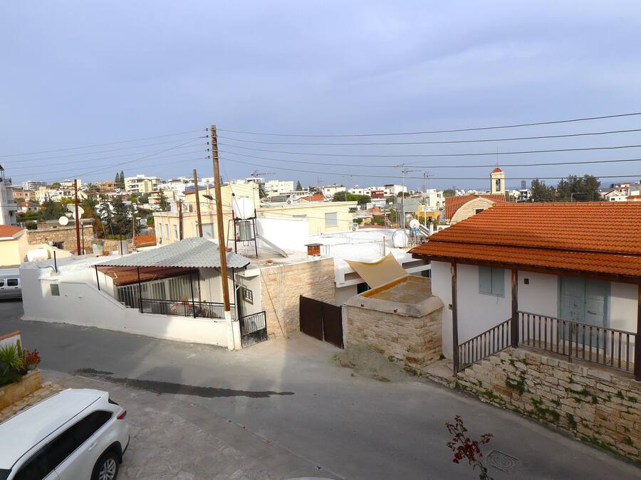 A residential area with white buildings, a street with parked cars, and a clear sky.