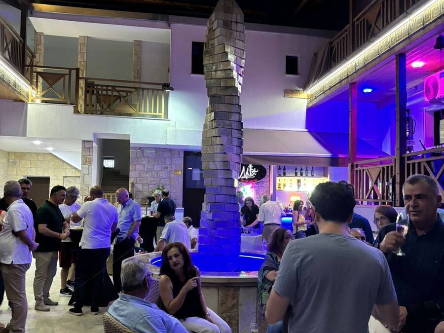 Un área de bar al aire libre con un pilar de piedra, asientos de mimbre y mucha gente.