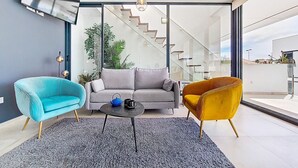 A modern living room with a grey sofa, a blue armchair, and a yellow armchair, a round coffee table, and a staircase leading to an outdoor area. - Penthouse apartment with pool views (Mar de Cristal)