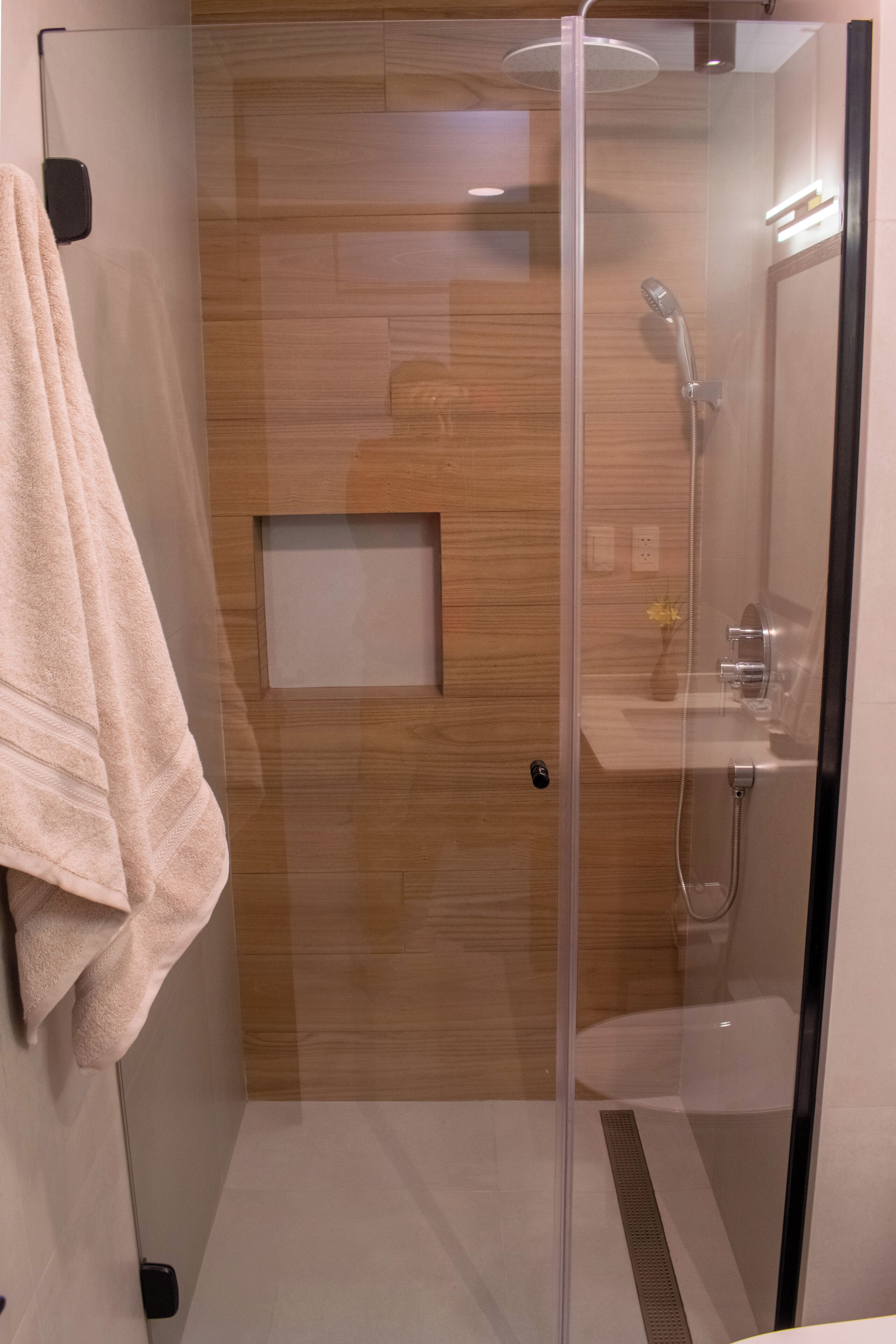A modern shower room with a glass door, wooden panel wall, and a towel hanging on the wall.
