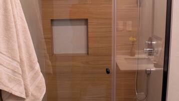 A modern shower room with a glass door, wooden panel wall, and a towel hanging on the wall.