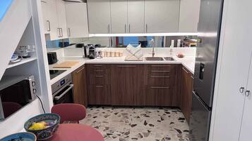 A compact kitchen with white cabinets, a stainless steel refrigerator, a built-in oven, and a small dining area with a red table and two bowls.