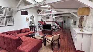 A spacious living area with a red sofa, wooden coffee table, and a TV. A staircase leads to an upper level.