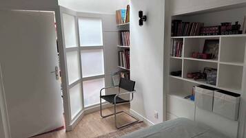 A room with a bed, a chair, a bookshelf, and a window.