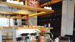 Een restaurantinterieur met een bar, houten tafels, stoelen en een potplant.