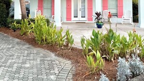 A two-story house with a tiled roof, a covered porch with red shutters, and a paved driveway.