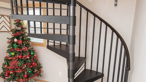 A black spiral staircase with a Christmas tree decorated with ornaments and a garland.