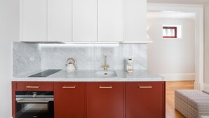 A modern kitchen with a marble countertop, a kettle, a coffee maker, and red cabinetry. - GuestReady - Downtown City Apartments - 2F (Porto)