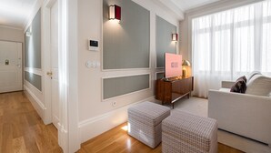 A modern hotel room with a wooden floor, a white sofa, a console table with a 'GUEST READY' sign, and a large window with sheer curtains. - GuestReady - Downtown City Apartments - 2F (Porto)