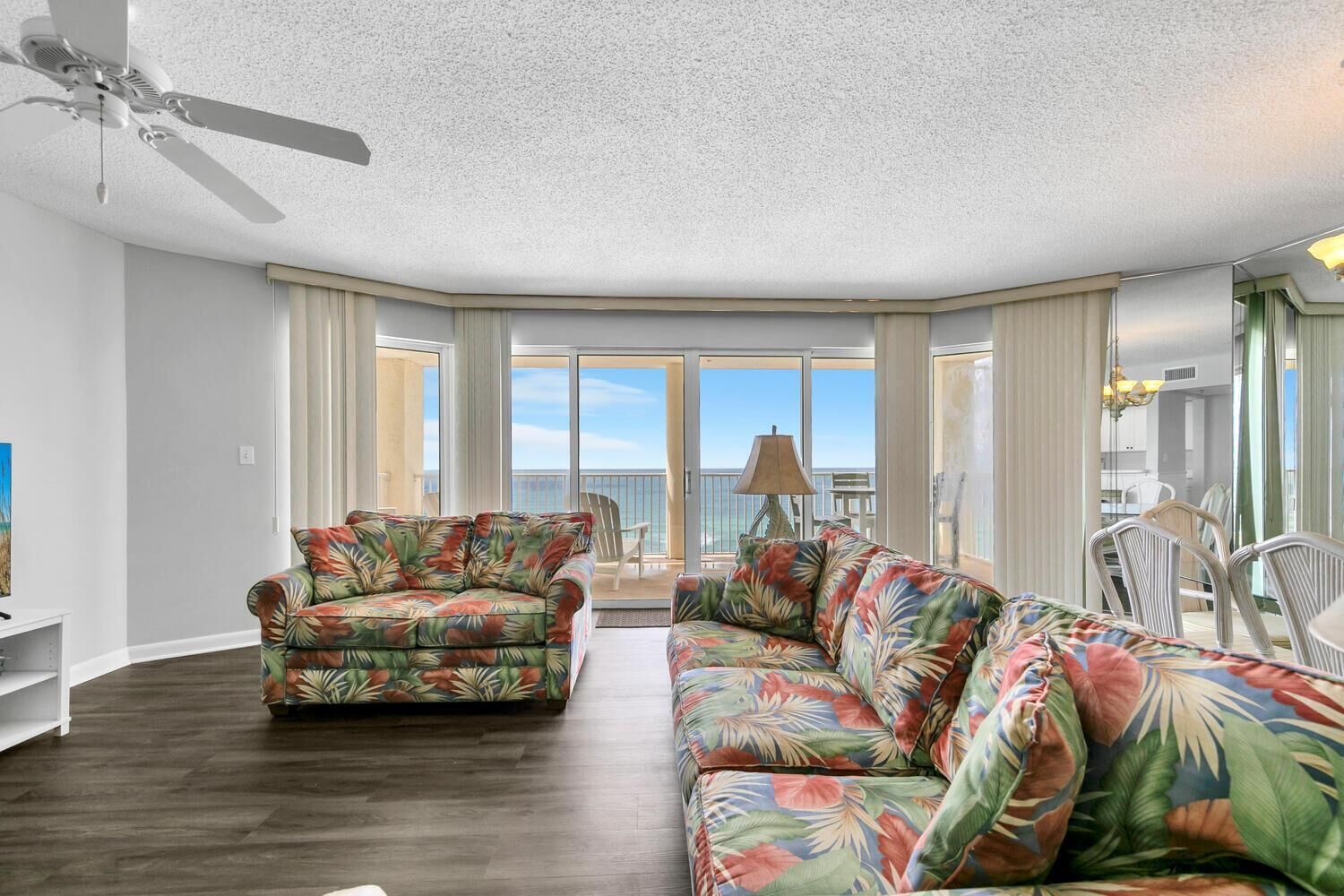 A spacious living room with a ceiling fan, a large window, and a view of the ocean.