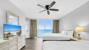 Habitación de hotel con cama, televisión, ventilador de techo, lámpara y vista al océano.