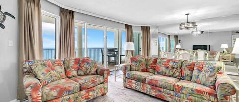 A spacious living room with two floral-patterned sofas, a ceiling fan, and a dining area with white chairs.