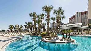Una piscina con palmeras y sillas de descanso, rodeada por un edificio de hotel.
