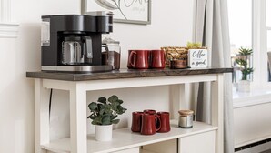 Un piano di lavoro in cucina con una macchina del caffè, tazze rosse, una pianta in vaso e un cartello con la scritta ‘Il caffè è sempre una buona idea.’