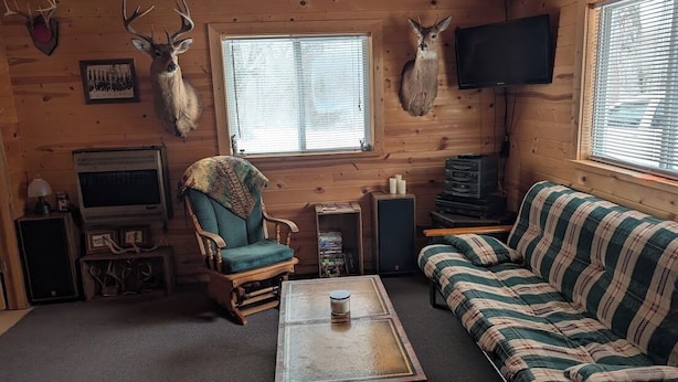 Interior acogedor de una cabaña con detalles de madera, un sofá, una silla, una mesa y monturas de animales.