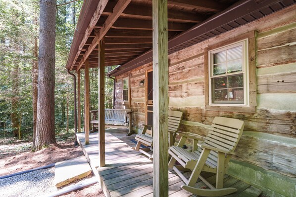 A wooden cabin with a porch, rocking chairs, and a bench.