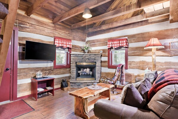 A log cabin interior with a stone fireplace, wooden furniture, and a television.
