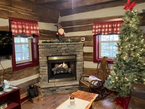 A cozy cabin interior with a stone fireplace, a Christmas tree, and a rocking chair.