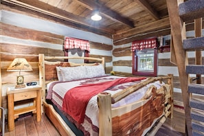 A rustic wooden cabin room with a bed, a nightstand, a window with curtains, and a wooden ladder.