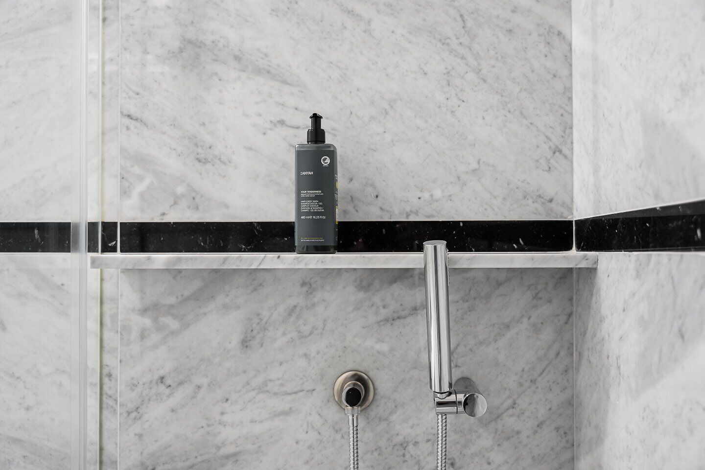 A bathroom with a marble wall, a black and white striped shelf, and a handheld showerhead.