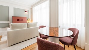 Una sala de estar moderna con una mesa redonda de vidrio, dos sillones tapizados, un sofá y una obra de arte enmarcada en la pared.