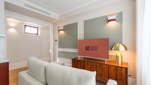Una habitación de hotel moderna con una televisión de pantalla plana grande sobre un mueble de madera, un sofá y una lámpara.