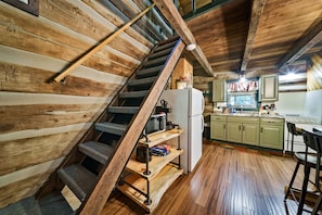 Interior rústico de una cabaña con escalera de madera, zona de cocina y comedor.
