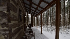 Une cabane en rondins avec un porche couvert et, en arrière-plan, une forêt enneigée.