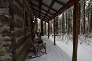 A log cabin with a covered porch and a snow-covered forest in the background.