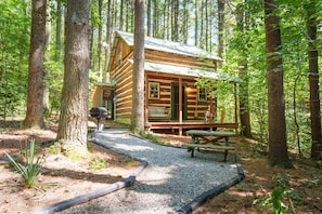 Una cabaña de troncos con un porche y una mesa de picnic, rodeada de árboles.