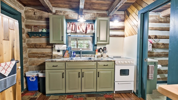 Une cuisine rustique avec des murs en bois, une étagère en pierre, une fenêtre avec des rideaux et un poêle.