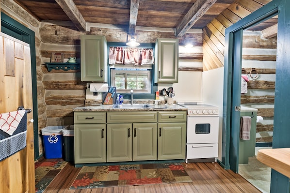 Una cocina rústica con paredes de madera, un estante de piedra, una ventana con cortinas y una estufa.