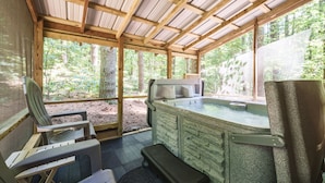 Une cabane en bois dotée d’un bain à remous, d’un coin salon et de grandes fenêtres donnant sur une forêt.