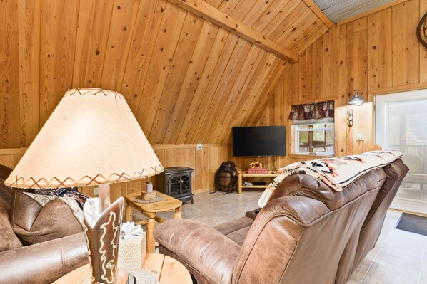 A cozy wooden interior with leather sofas, a television, and a fireplace.