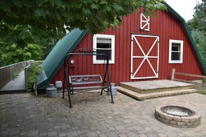 A red barn with a green roof, a wooden bench, a fire pit, and a metal bench with a metal sculpture.