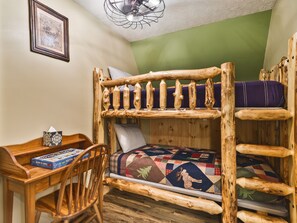 A bunk bed with a wooden frame, a desk with a chair, a quilted bedspread, and a framed picture on the wall. - Woodland view-Hitchin' Post (Laurelville)